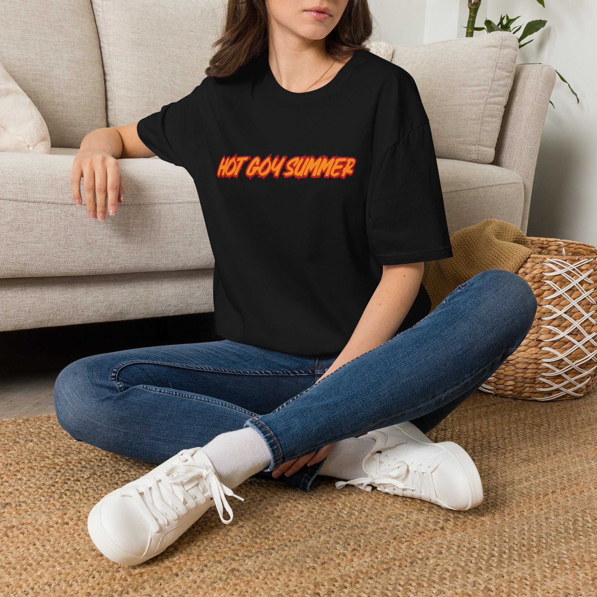 Person wearing a black t-shirt with the words HOT GOY SUMMER with yellow text sitting on the floor in a living room.