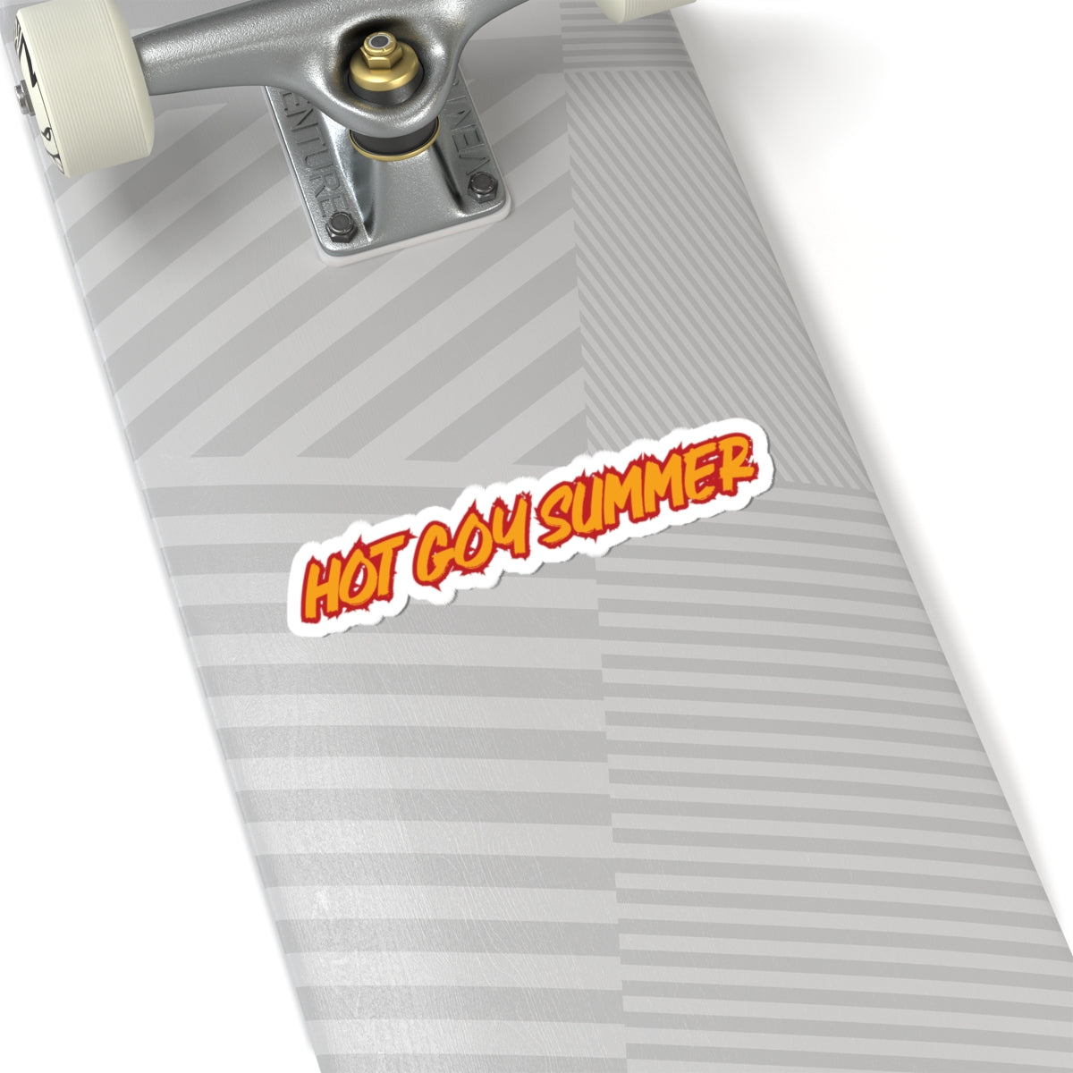 A close-up of a skateboard deck with a gray and white striped chevron pattern, featuring a die-cut sticker that reads 'HOT GOY SUMMER' in orange and white with a black outline. The skateboard includes a silver metal truck and cream-colored wheels, set against a clean white background.